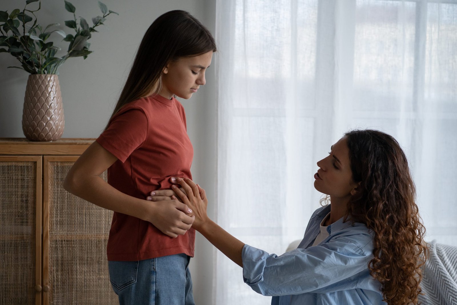 Depressed unhappy teenage girl near mom holding stomach complaining of pain after eating fast food