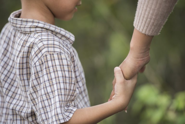 Close up of happy mum and son holding hand in a park. Family con