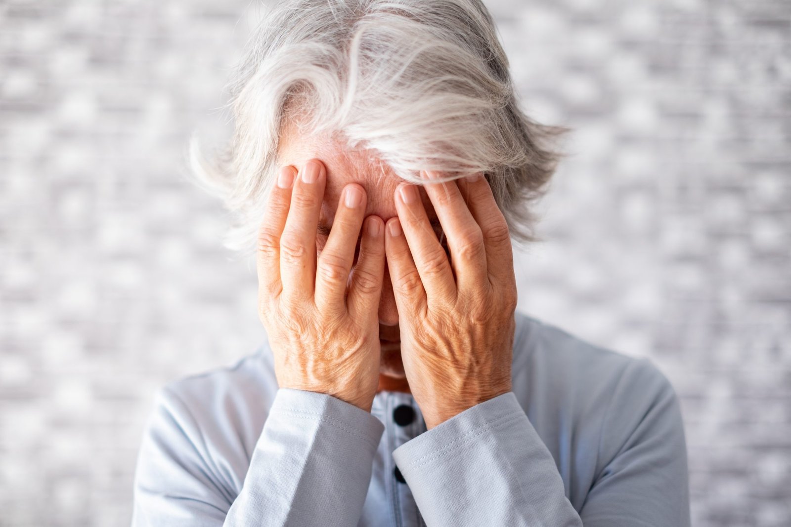 Frustrated depressed old woman covering face with hands and cryi