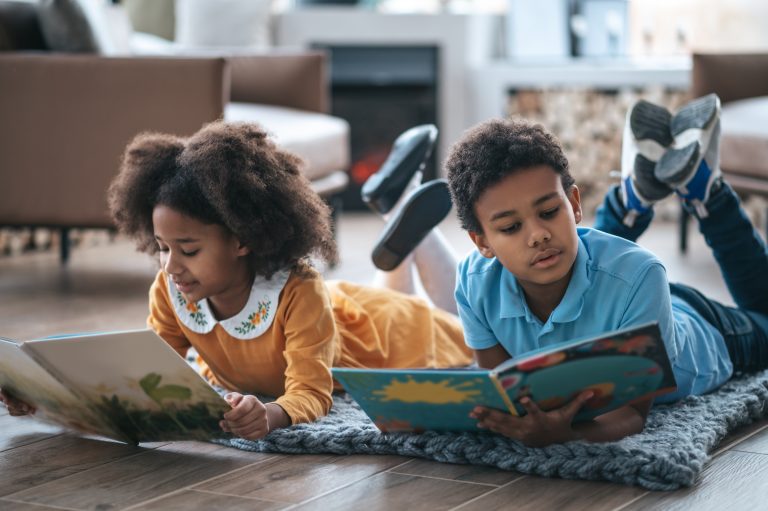 Two kids lying on the floor and reading a book