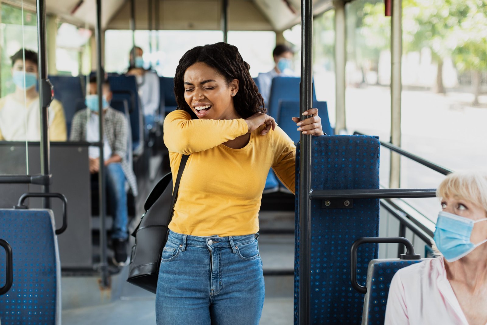 Black woman sneezing and coughing in elbow standing in bus