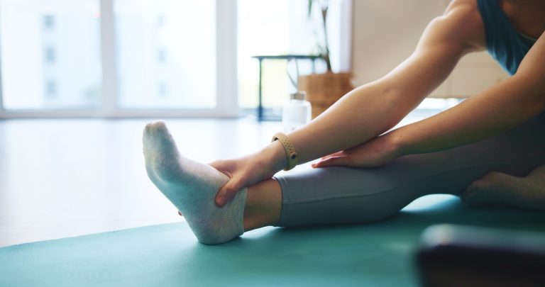 woman-hands-or-stretching-foot-on-mat-in-home-for-2024-10-15-03-42-14-utc--1-
