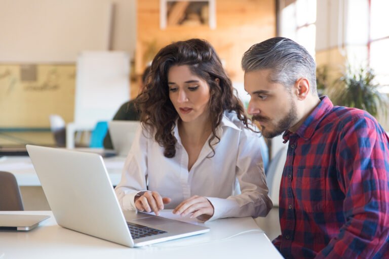 Serious coworkers discussing project and using laptop together